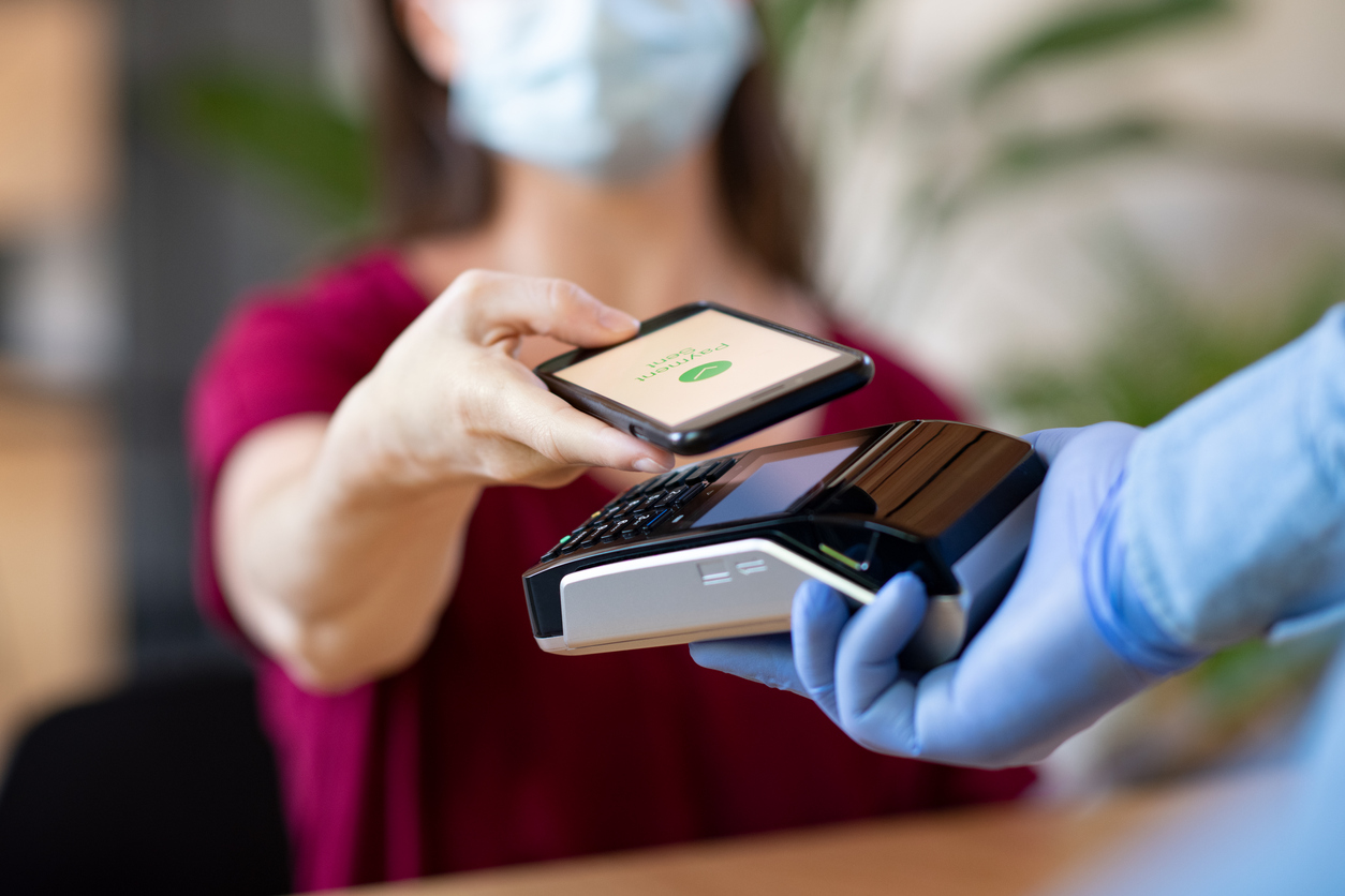 A masked woman making a contactless payment in a cafe