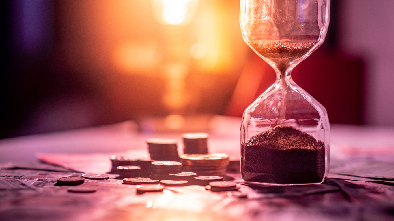 Hourglass on a table beside coins and banknotes