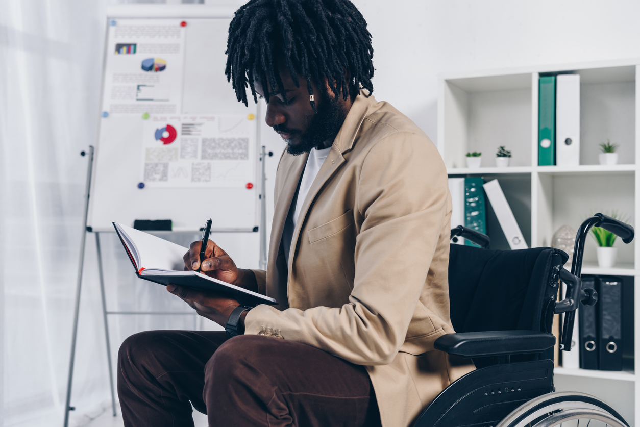 Disabled employee in a wheelchair writing in a notebook