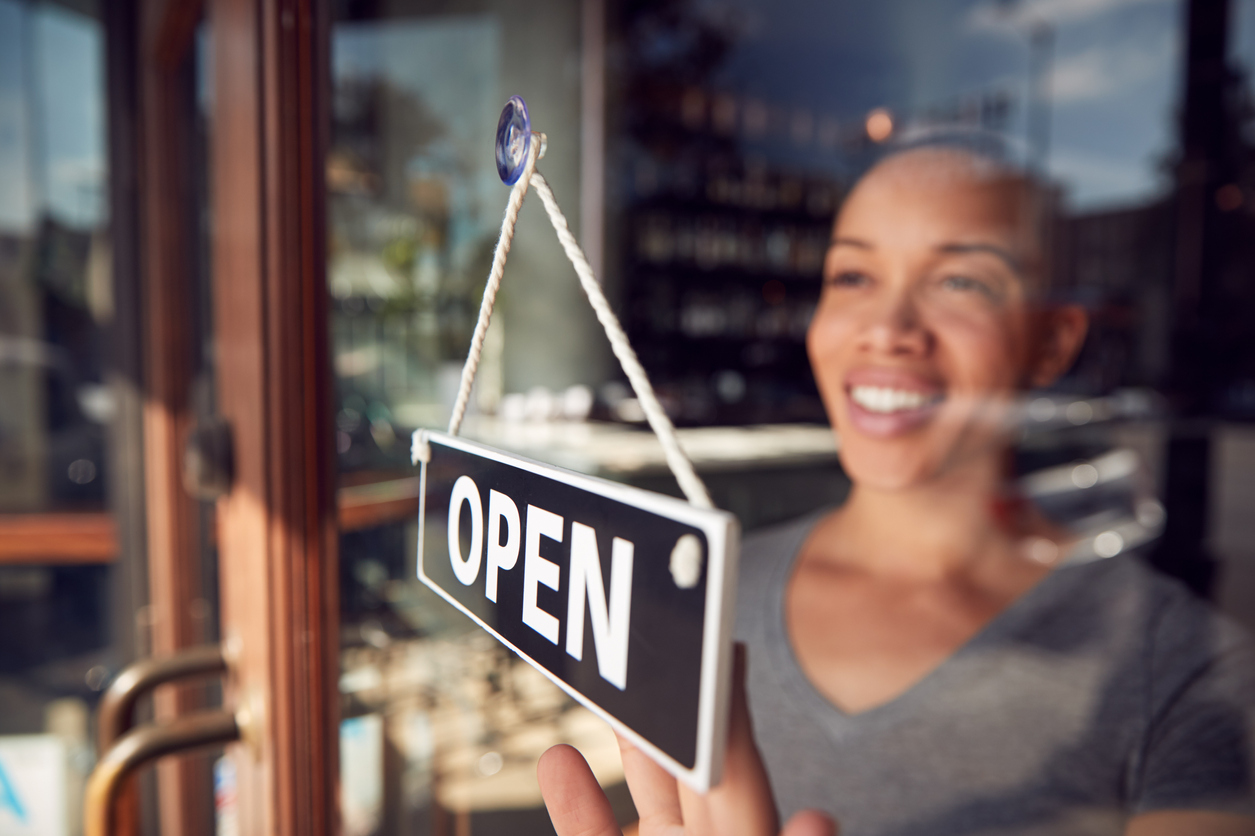 Young woman in coffee shop turning "Open" sign