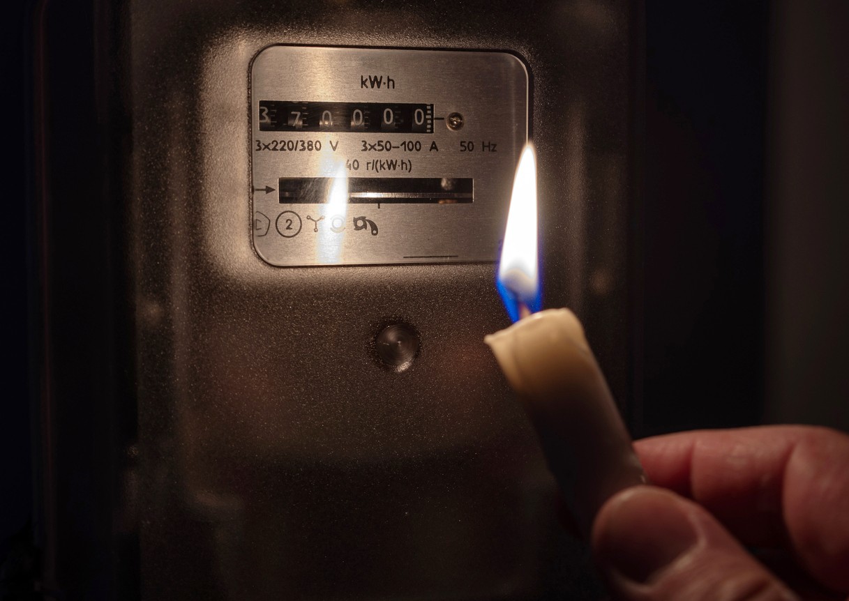 Electricity meter illuminated by the light of a candle; energy crisis