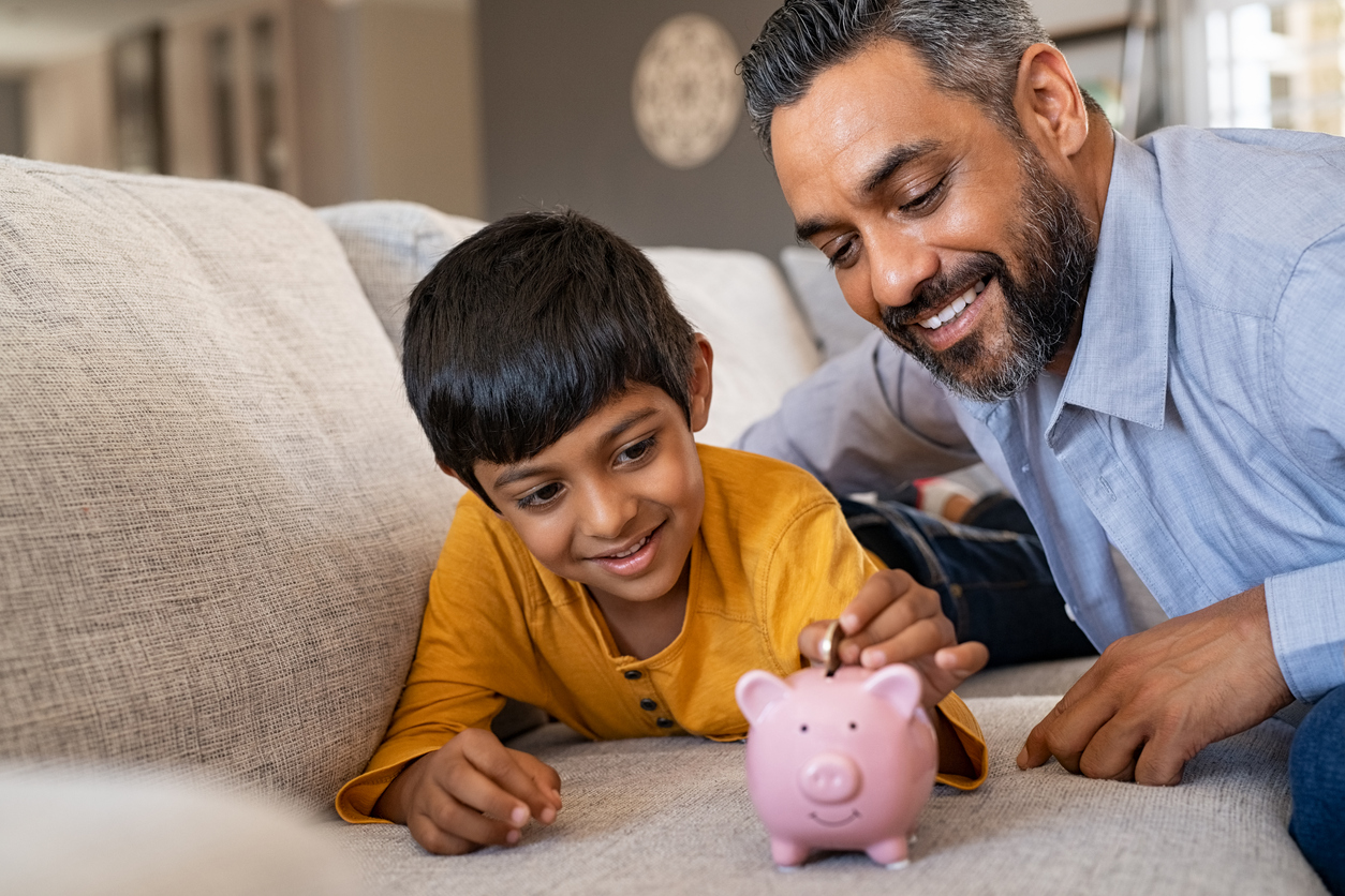 Young boy saving money with the help of father/guardian