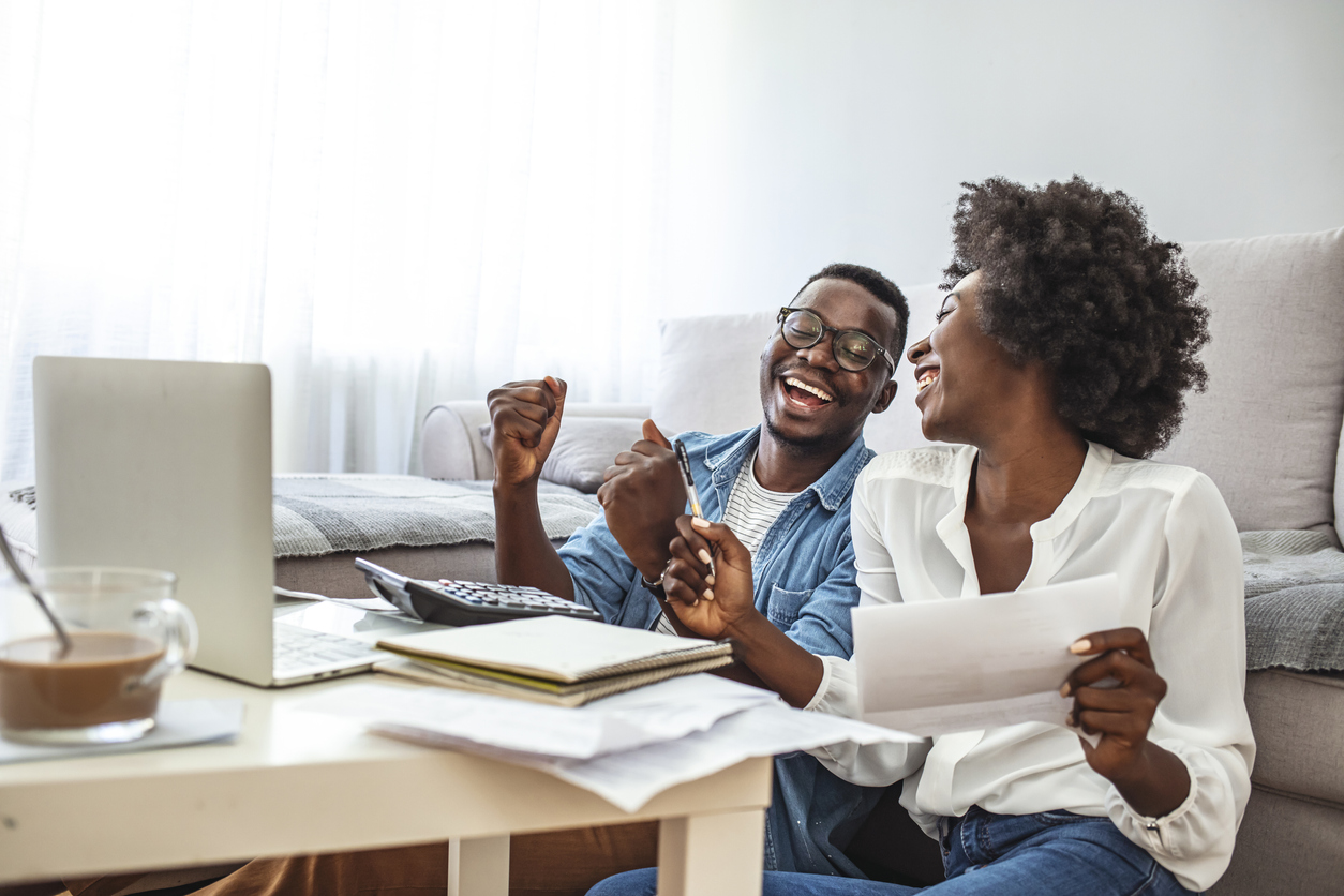 Family insurance concept. Positive black couple reading documentation at home, checking agreement details together. Young African Couple Sitting On Sofa Calculating Invoice