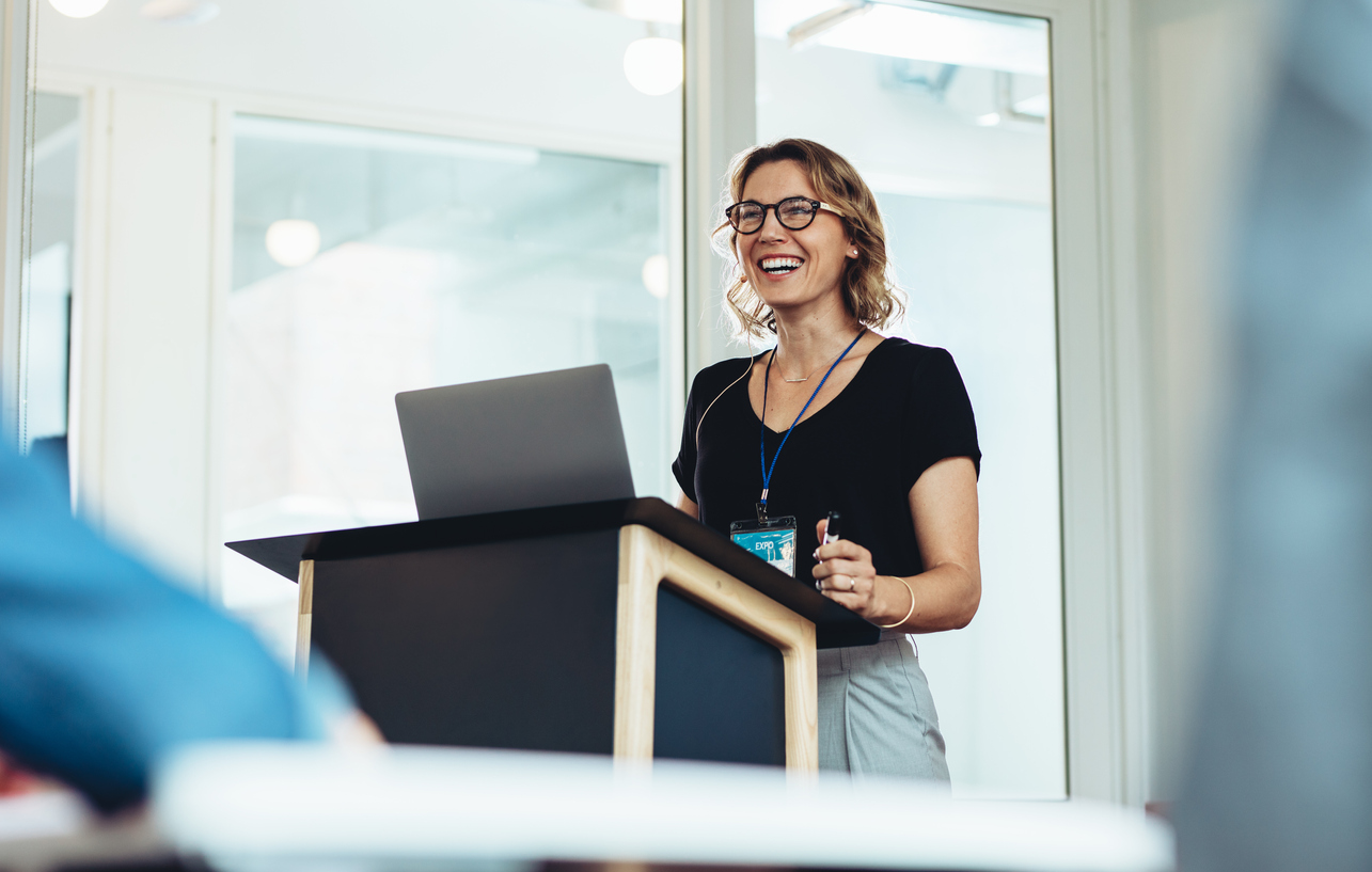 Businesswoman standing at podium with laptop giving a speech. Successful female business professional addressing a seminar.