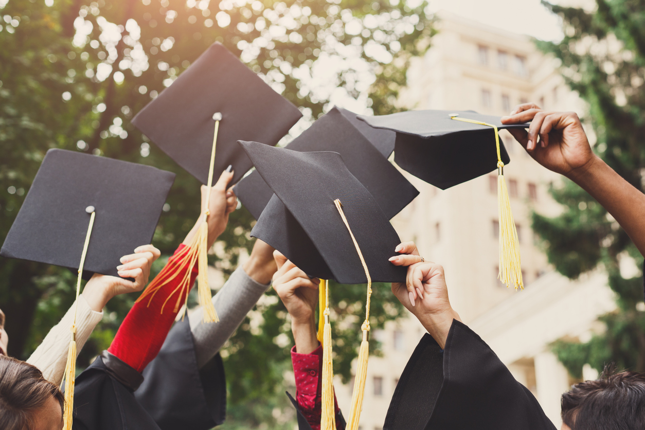 A group of multietnic students celebrating their graduation by throwing caps in the air closeup. Education, qualification and gown concept.