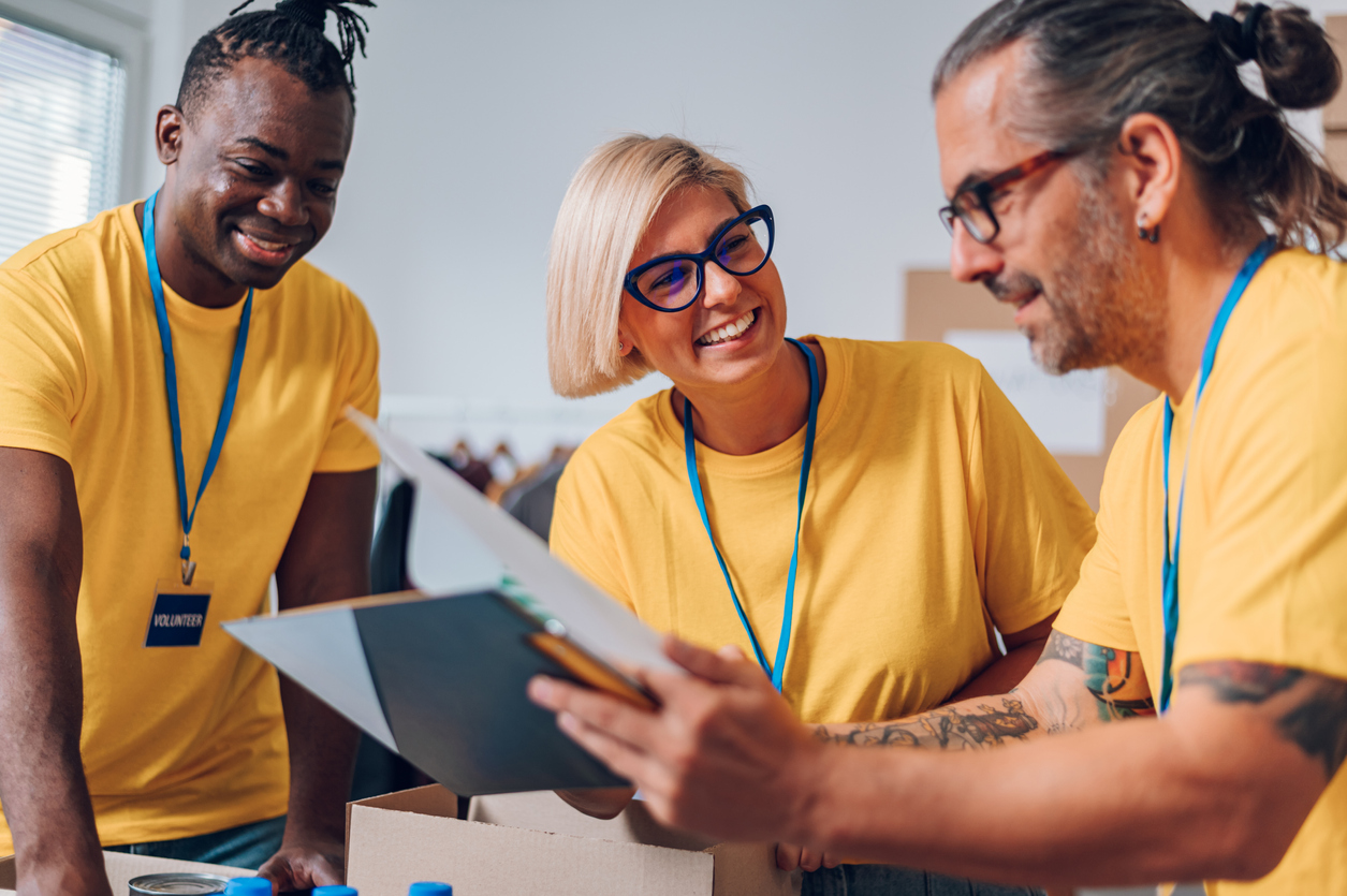 Group of diverse people working in charitable foundation. Happy volunteer separating donation stuff. Social workers making check list of the thins that are done. Copy space. Working as a team.