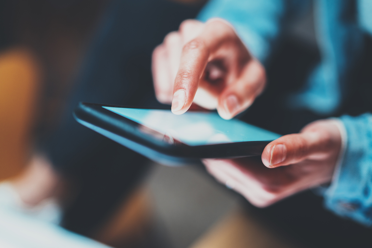 Closeup view of woman holding modern smartphone in hands.Girl typing on white touch mobile screen. Horizontal, blurred background, bokeh effects.Macro