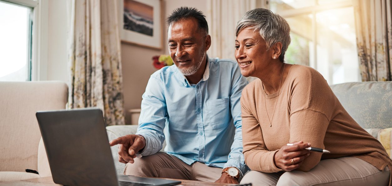 mature couple, sofa and laptop for planning finance, retirement funding and investment or asset management at home. elderly people or man and woman reading information on computer for pension savings