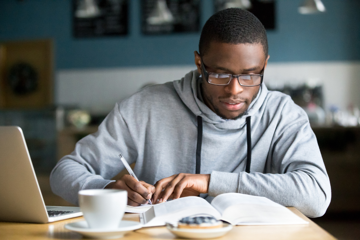 focused millennial african student making notes while studying in cafe