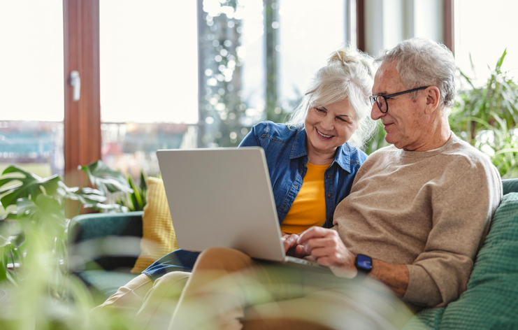 senior couple using laptop while sitting on sofa in living room at home