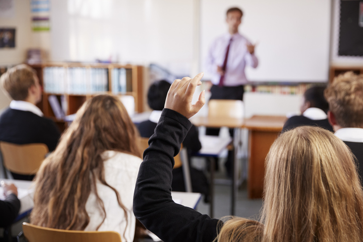 female student raising hand to ask question in classroom