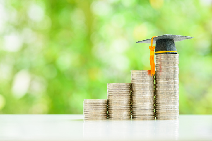 graduate study abroad, education concept : graduation cap sits atop stacks of coins, depicting bursaries and scholarships that provide financial assistance to students with no obligation to repay.