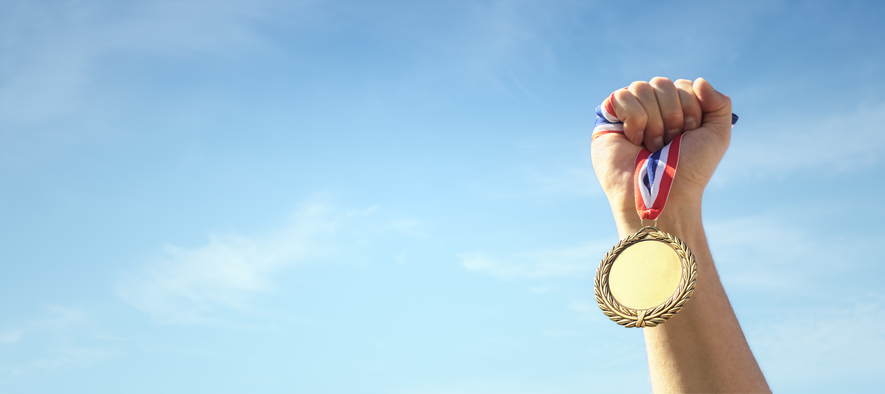 gold medal held in athlete hand raised against sky background