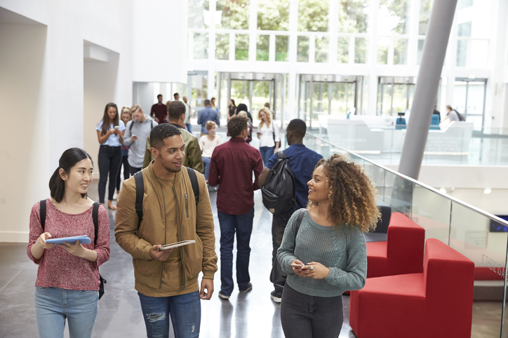 students holding tablets and phone talk in university lobby