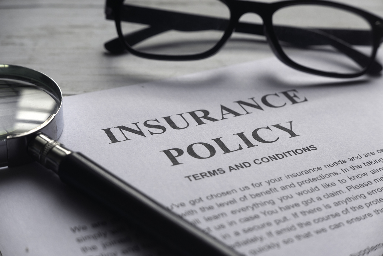 selective focus of magnifying glass,glasses and insurance policy letter on a white wooden background.