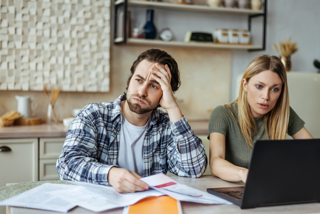 upset european millennial man with stubble and blonde woman pay bills and taxes with laptop in light kitchen