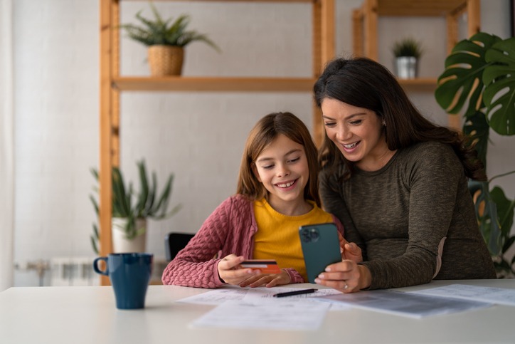 mother and daughter using smart phone and credit card, booking a flight together, planning a vacation.