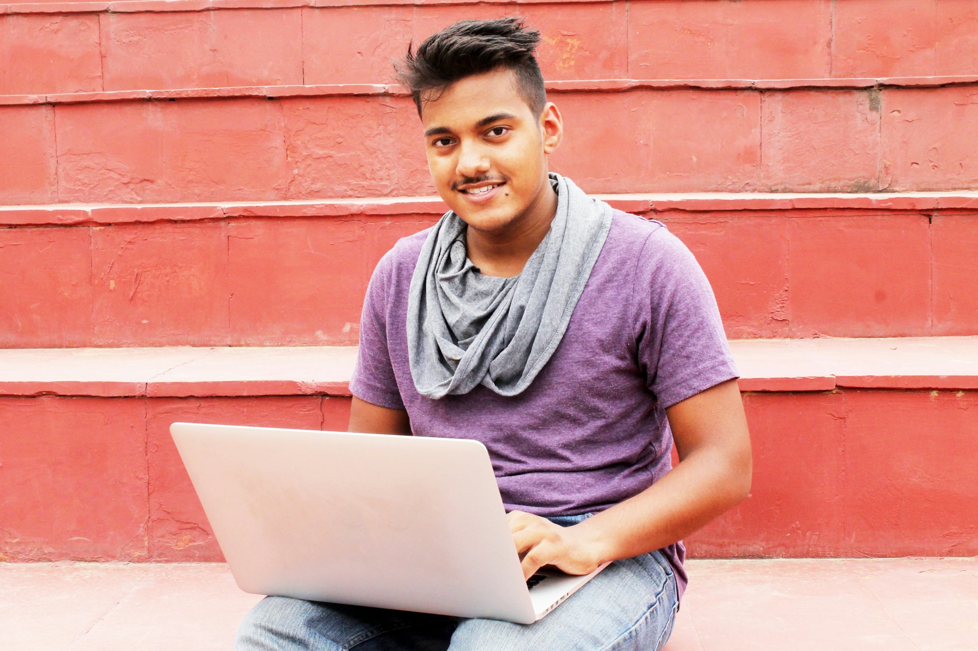 Portrait of a young man sitting outside with a laptop. He's looking at the camera.