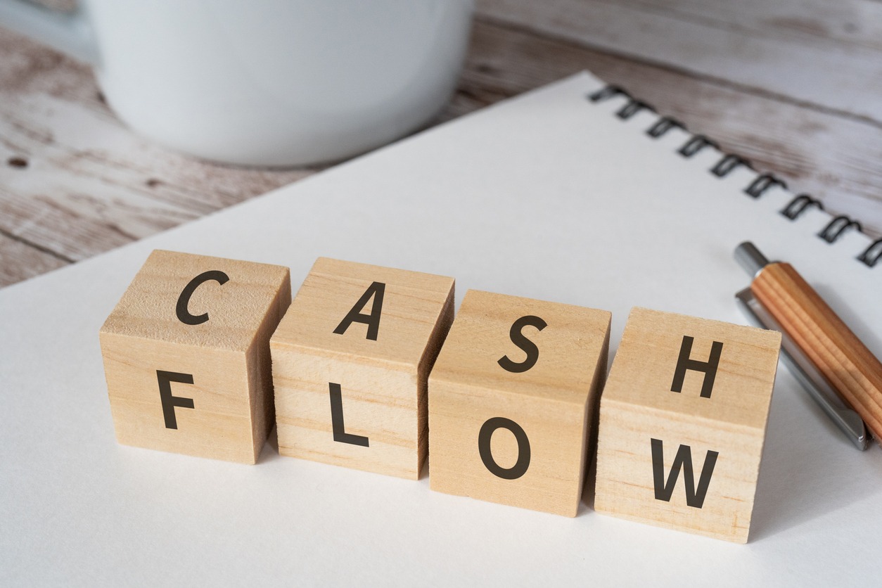 wooden blocks with "cash flow" text of concept, a pen, a notebook, and a cup.