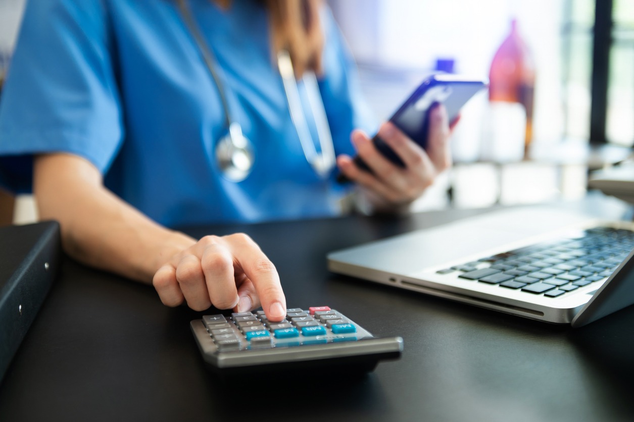 healthcare costs and fees concept.hand of smart doctor used a calculator and smartphone, tablet for medical costs at hospital in morning light