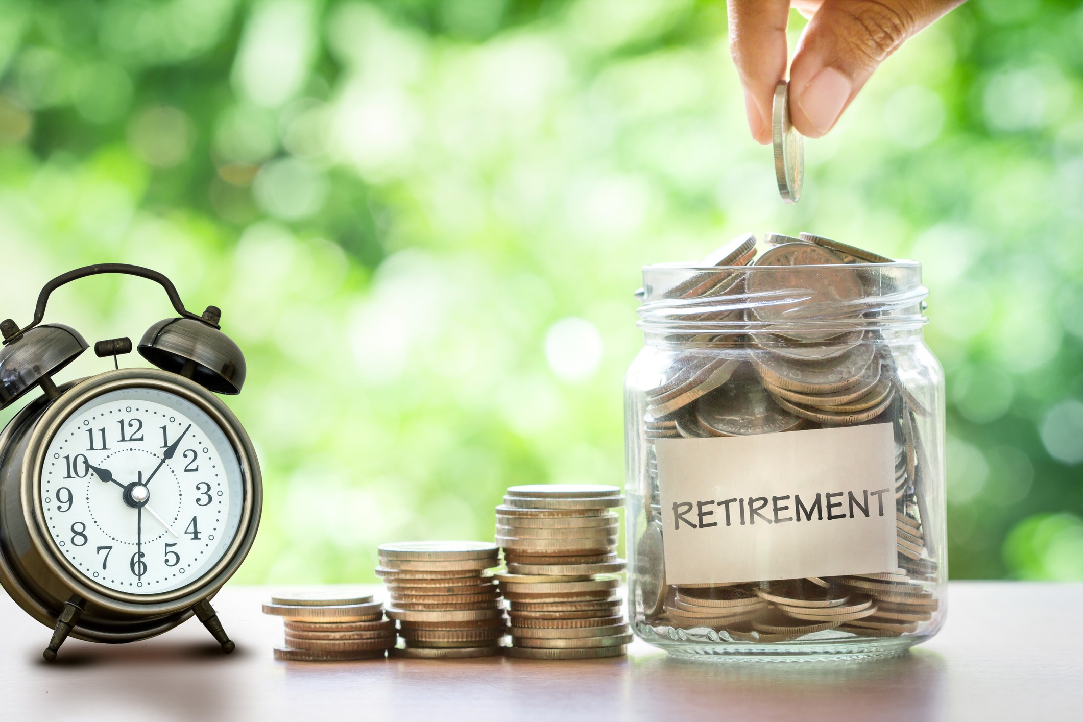 hand putting coins in glass jar with retro alarm clock